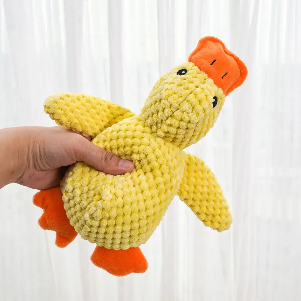 Hand holding a yellow plush duck toy with an orange beak against a white curtain background