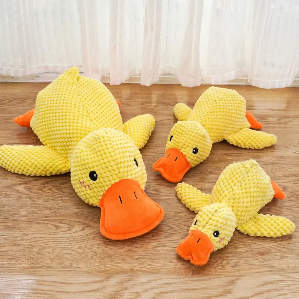 Three yellow duck plush toys with orange beaks on a wooden floor.