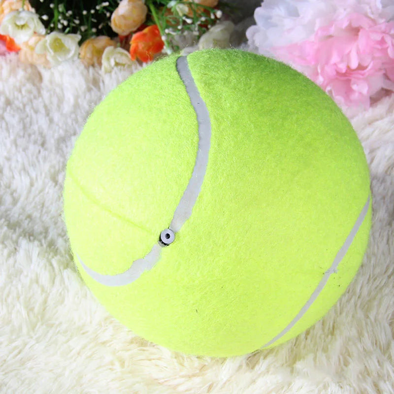 Yellow tennis ball with a white stripe on a fluffy white surface with flowers in the background showing where to pump the air
