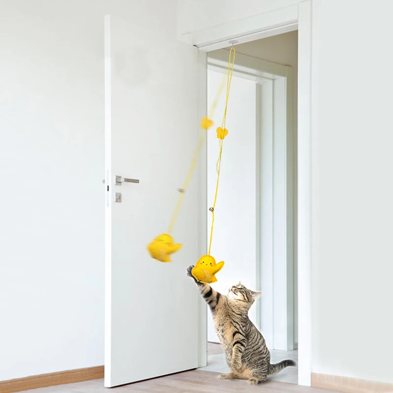 Cat playing with a yellow rubber duck toy attached to a string on a white door.